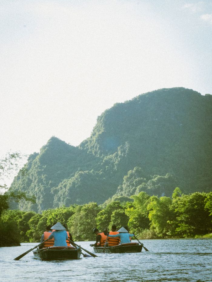 Tourists enjoy a calm river ride with stunning views of lush green mountains in Vietnam.