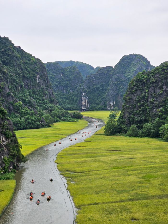 A stunning river weave through lush green valley with boats gliding, surrounded by towering mountains.