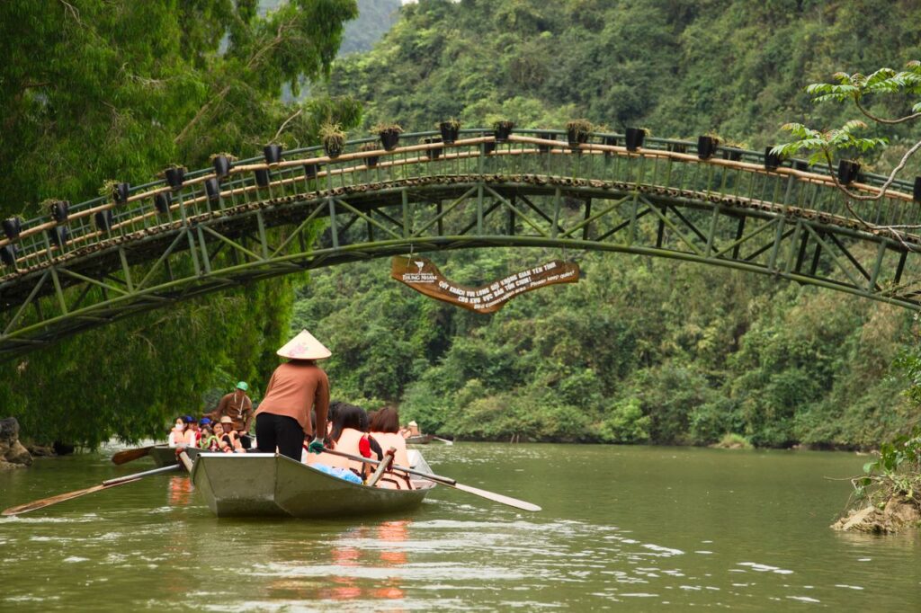 A peaceful boat ride under a scenic bridge in a lush, green Asian landscape. Captures tranquility.