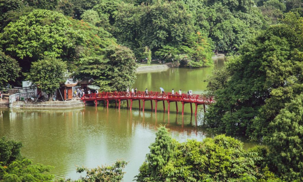 A scenic red bridge spans a calm river in a lush, green forest setting, inviting exploration.